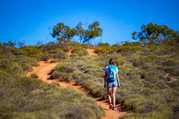 fit girl with backpack hiking uphill on red rocks in cape range national park in western australia,...