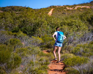 Naklejka premium fit girl with backpack hiking uphill on red rocks in cape range national park in western australia, hiking in australian outback, australian desert