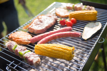 Tasty BBQ food cooking on sunny day. Juicy raw meat, mushrooms and yellow corn grilling. BBQ, cooking, food concept
