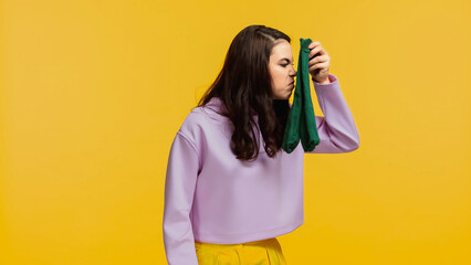 brunette woman in purple sweatshirt smelling stinky socks isolated on yellow - obrazy, fototapety, plakaty