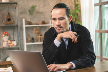 Asian freelancer working on laptop at desk in co-working space, businessman talking to customer with online communication system.