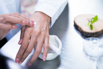 A young scientist is mixing skin creams with natural ingredients. She tests skin serums in a cosmetic laboratory.