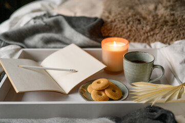 cup of coffee and cookies, burning aroma candle open book with pencil on cozy grey blanket on bed on an autumn day