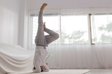 senior age woman attractive white and gray sportswear practicing and exercise in head stand yoga style in room ,king of pose yoga lesson.
