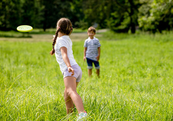 Siblings throwing flying disc playing in the park together