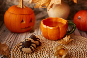 Obraz na płótnie Canvas Aesthetics Halloween spider cookies and cup of tea among pumpkins and fragrant leaves