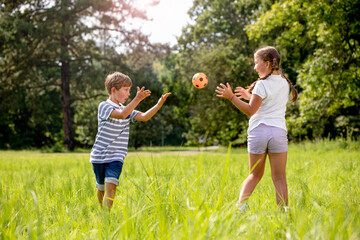 Fototapeta premium Happy siblings throwing ball and playing on green grass in park