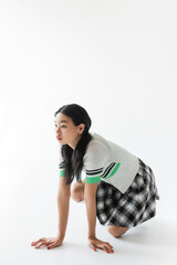 Stylish asian model kneeling and looking away on grey background
