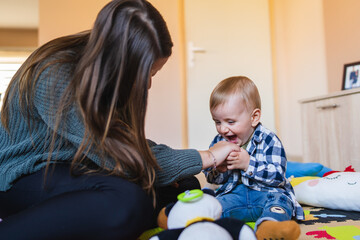 A mother and son are playing on kids carpet with toys baby is playing and sitting on the ground with toys