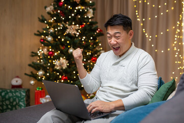 Man celebrating new year at home and christmas, asian got good news online reading from laptop and...