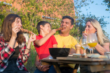 Caring family sitting around table. Mid adult parents and children looking at camera, eating meat, son feeding father. BBQ, cooking, food, family concept