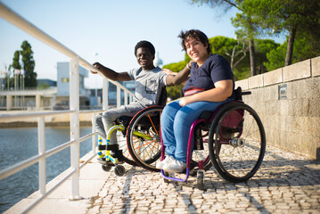 Tender biracial couple having walk on summer day. African American man and Caucasian woman in wheelchairs on embankment, touching each others shoulders. Love, relationship, happiness concept