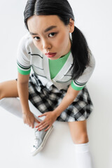 Overhead view of brunette asian woman in cropped cardigan looking at camera on grey background