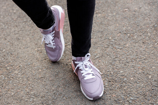 cropped image of female legs in shoes. Woman in black jeans and pink sneakers stands on pavement