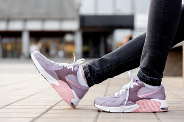 woman in black jeans and sneakers sits on bench. Womens legs in pink sneakers close up