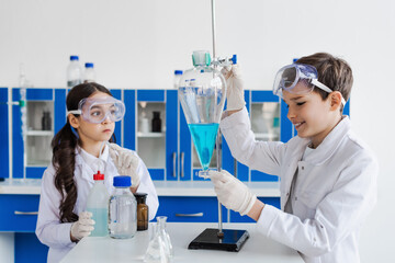 smiling boy holding flask with liquid near serious girl in goggles.