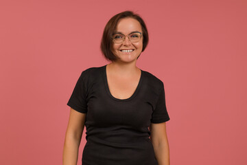 cheerful smiling woman in big glasses and a black t-shirt on a pink background looking at the camera