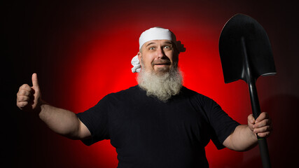 cheerful man with a beard with a bandage on his head holds a shovel in his hand and shows a thumbs...