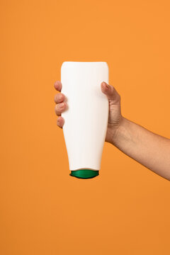 white bottle with a green cap upside down in a hand on a yellow background