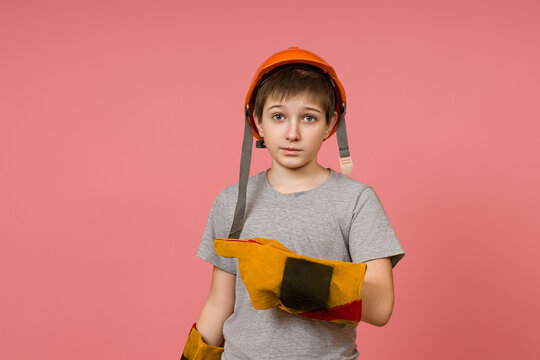a child in a hard hat and construction gloves points a finger to the side on a pink background