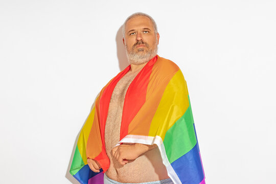 A man wrapped an lgbt flag around his neck and looks contemptuously at the camera.