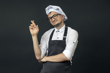 the chef in a black apron on a black background crossed his fingers in his palm. riddle concept.