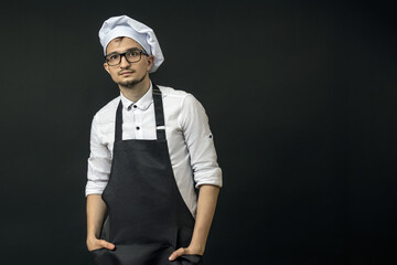 a chef in a black apron stands straight and looks at the camera with his palms in his apron pockets. chefs posing concept.