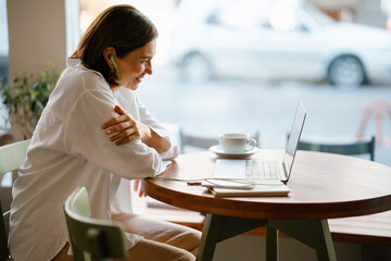 White mature woman working with laptop while sitting in cafe