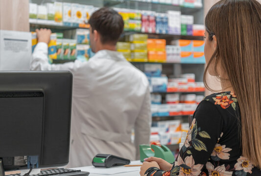 Farmac&eacute;utico cogiendo medicinas en la estanter&iacute;a, con clienta irreconocible en la farmacia.