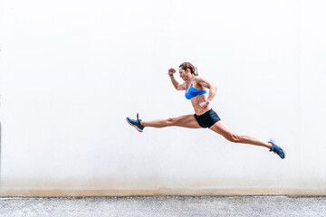 Strong sportswoman leaping against wall