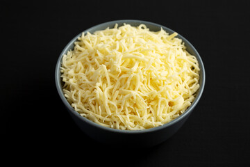 Shredded Mozzarella Cheese in a Bowl on a black surface, side view.