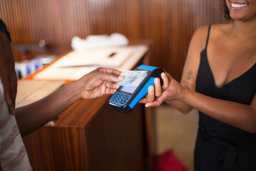 Close-up of male and female hands during contactless service. African American customer paying with card after buying clothes and seller holding credit card reader. Business and modern service concept