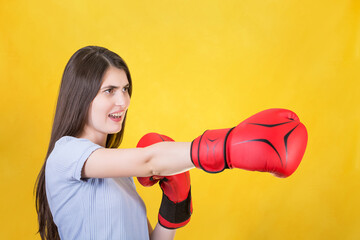 Angry young woman with red boxing gloves stands in fighting position, punching with hand. Portrait...