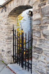 Selective focus vertical side view of stone wall with arched entryway with iron gate in the old town, Quebec City, Quebec, Canada
