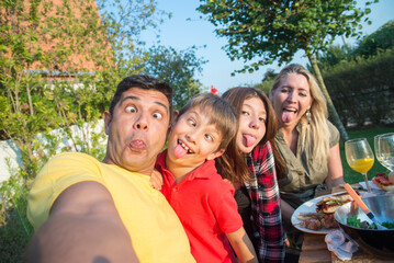 Funny family taking selfie at BBQ party. Mid adult parents and daughter sitting around table, making faces, laughing. BBQ, social media, food, family concept