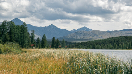 Atmospheric view of a mountain lake with camping on the shore in a coniferous forest against the backdrop of mountains and a dramatic cloudy sky