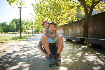 Portrait of Asian father and kid having fun with skateboard. Smiling man sitting on skateboard and...