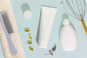 Hair cosmetics. Hair care card with shampoo and conditioner bottles with comb, massager for head and eucalyptus leaves on a blue background. Mock up of natural beauty products for hair