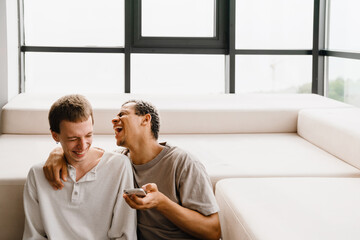 Happy gay couple using cellphone and laptop while resting at home
