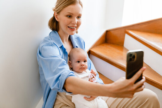 White blonde woman smiling and taking selfie photo with her baby