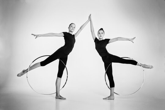 a two girls from rhythmic gymnastics in a bodysuit show a deflection holding a hoop on their feet and holding hands