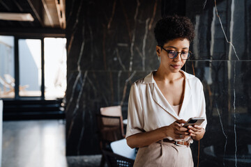 Happy black businesswoman using cellphone while working in office lobby