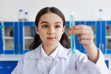 brunette girl in white coat holding blurred test tube in lab.