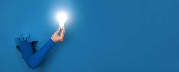 hand holding light bulb over blue background, panoramic layout