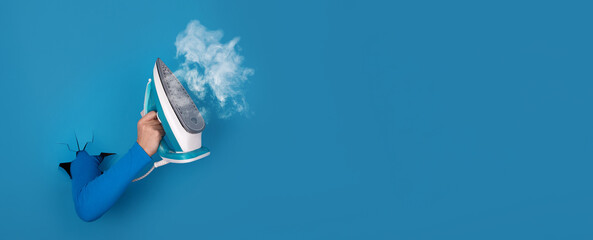 modern iron with steam in hand over blue  background, panoramic layout