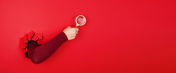magnifier in hand over red background, search concept, panoramic layout