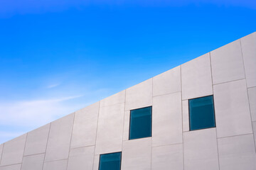 Low angle and side view of glass windows on modern white concrete building wall against blue sky,...