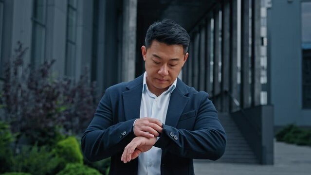 Angry worried middle-aged man waiting taxi worry about lateness. 40s Asian Korean sad dissatisfied businessman male frustrated entrepreneur wait meeting outdoors in city nervous looking at wristwatch