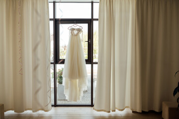 A beautiful and delicate dress hangs by the window