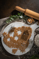 Making christmas gingerbread cookies. Raw dough in shape of gingerbread man, christmas tree, star, snowflakes on paper on tray on rustic table with rolling pin. Preparing for baking